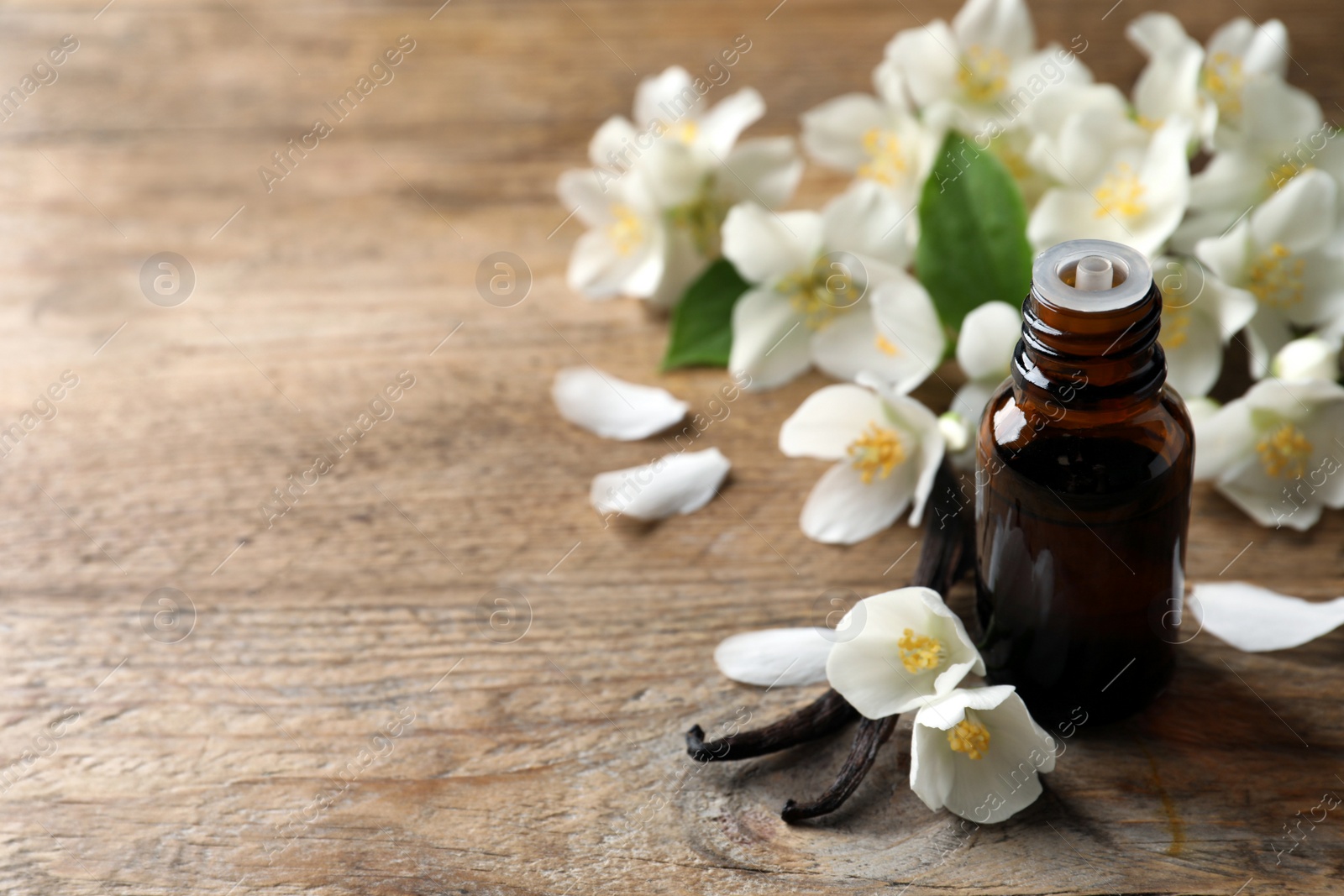 Photo of Jasmine essential oil and fresh flowers on wooden table, space for text