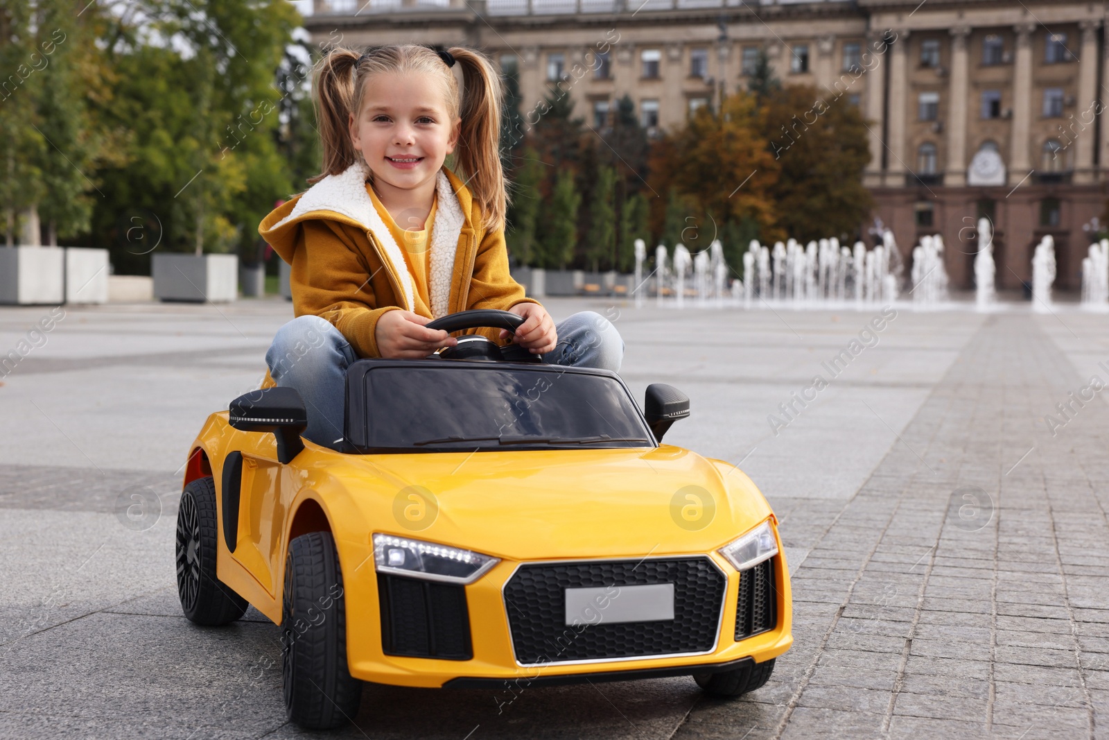 Photo of Cute little girl driving children's car on city street
