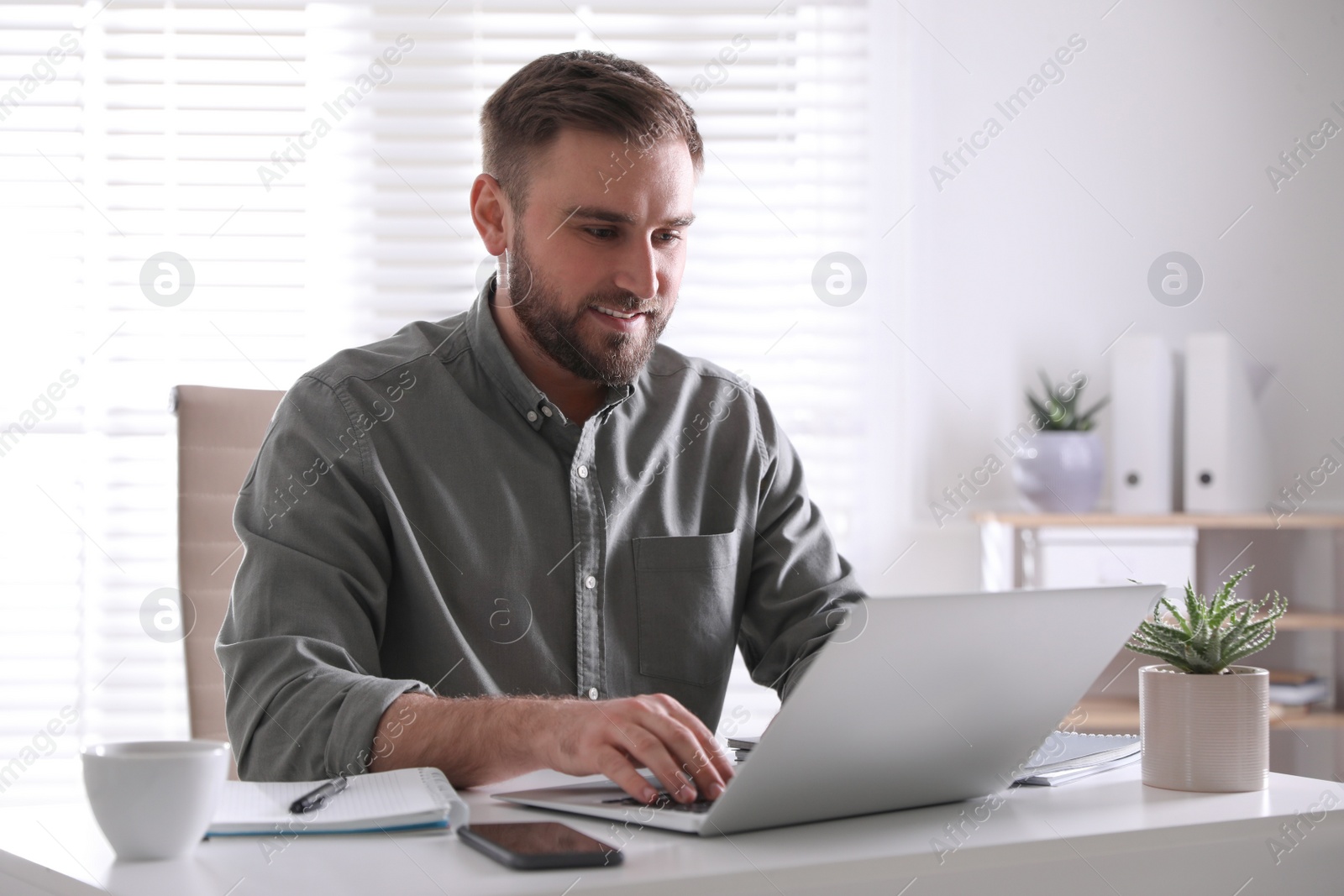 Photo of Young man working on laptop at table in office