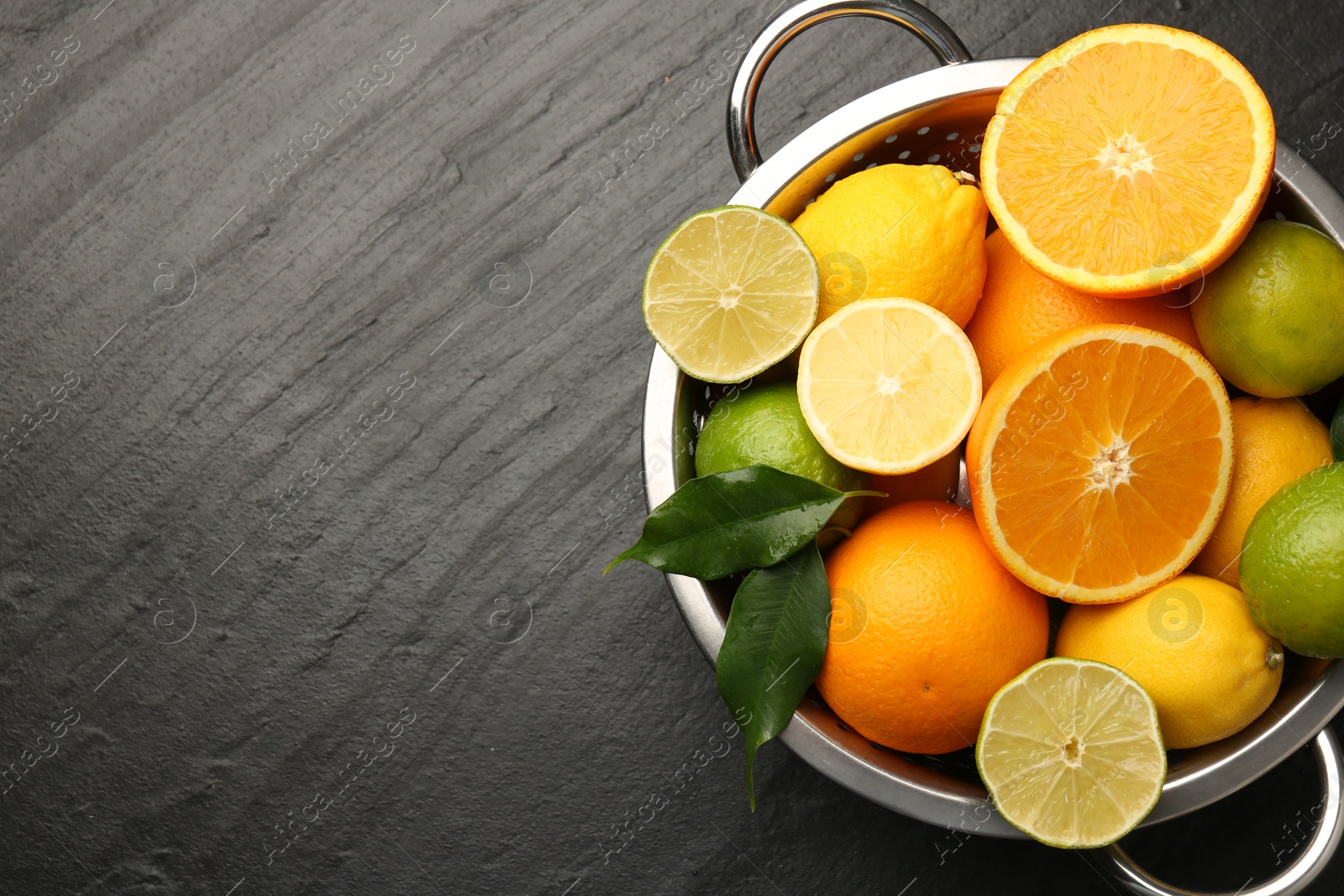 Photo of Fresh citrus fruits in colander on dark textured table, top view. Space for text