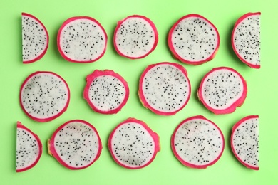 Photo of Slices of delicious dragon fruit (pitahaya) on green background, flat lay