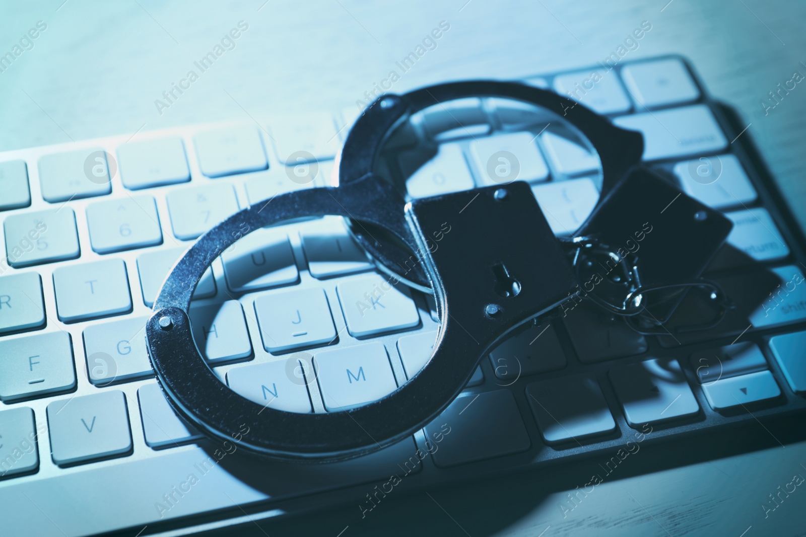 Photo of Handcuffs and computer keyboard on table, closeup. Cyber crime