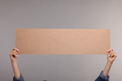 Woman holding blank cardboard banner on grey background, closeup. Space for text