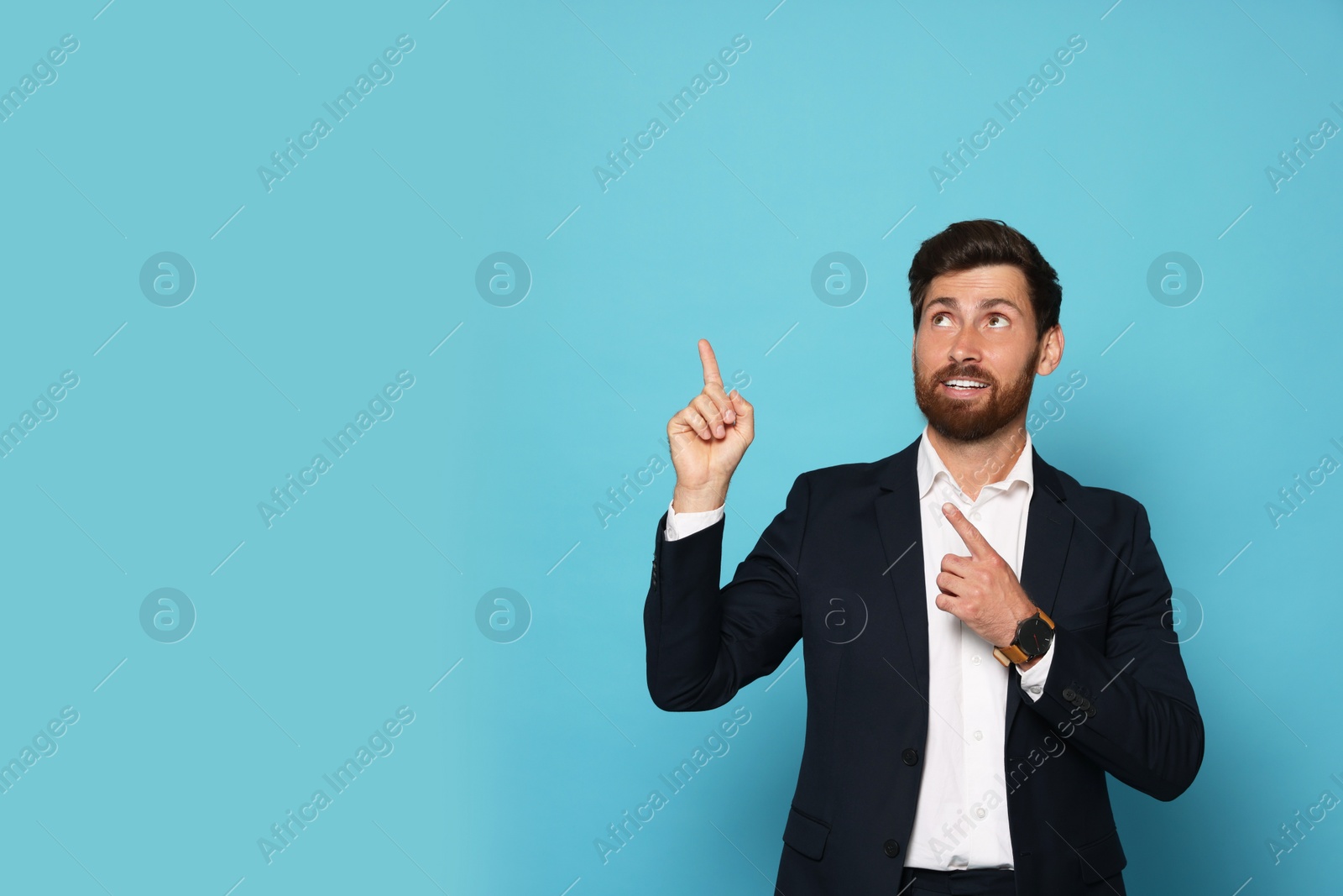 Photo of Smiling bearded man pointing index fingers up on light blue background. Space for text