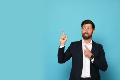 Photo of Smiling bearded man pointing index fingers up on light blue background. Space for text
