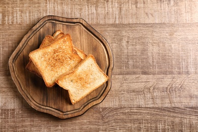 Photo of Board with toasted bread on wooden background, top view