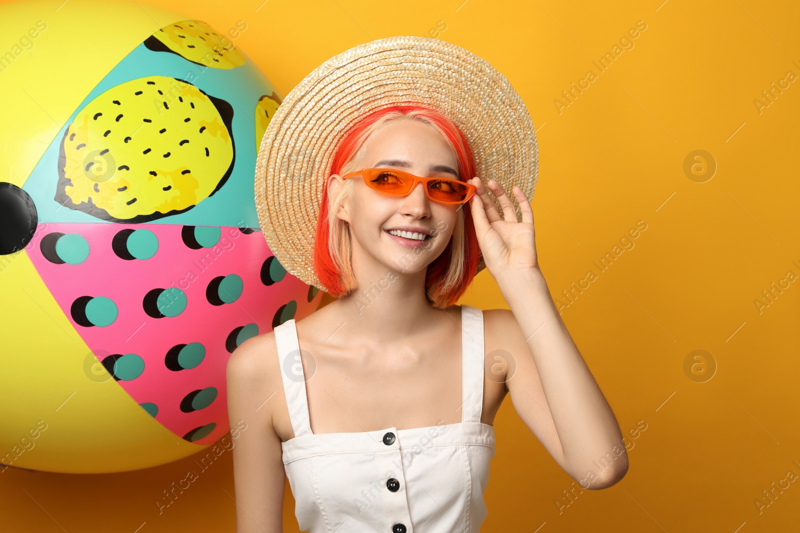 Photo of Beautiful young woman with bright dyed hair and inflatable ball on orange background