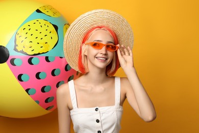 Beautiful young woman with bright dyed hair and inflatable ball on orange background
