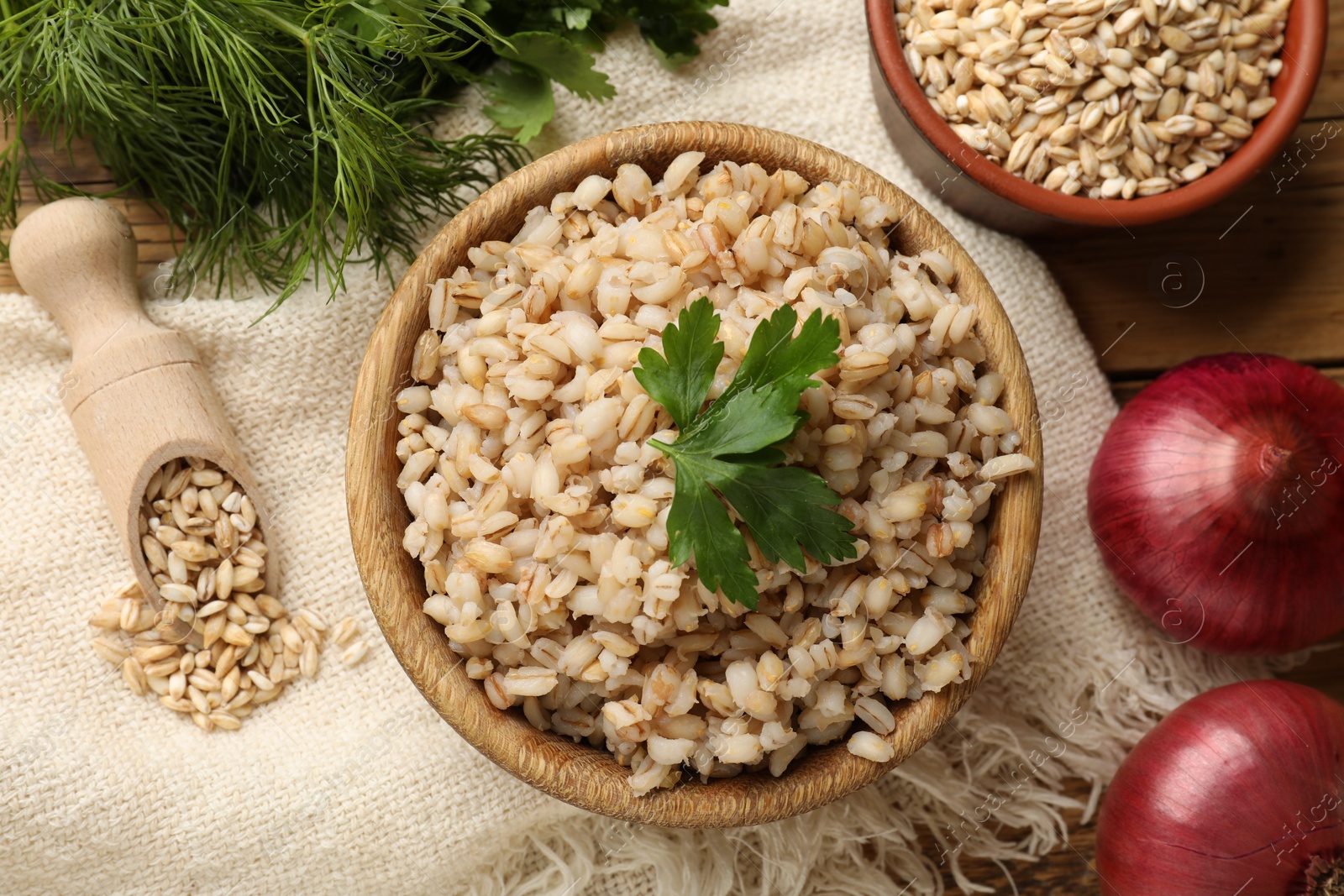 Photo of Delicious pearl barley with parsley in bowl served on table, flat lay