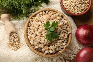 Photo of Delicious pearl barley with parsley in bowl served on table, flat lay