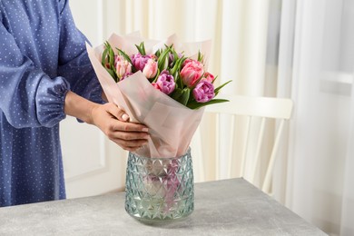 Photo of Woman putting bouquet of beautiful tulips in vase indoors, closeup. Space for text