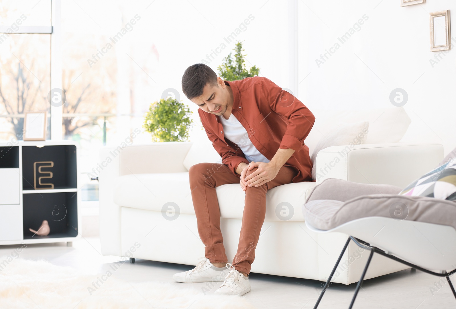 Photo of Young man suffering from knee pain at home