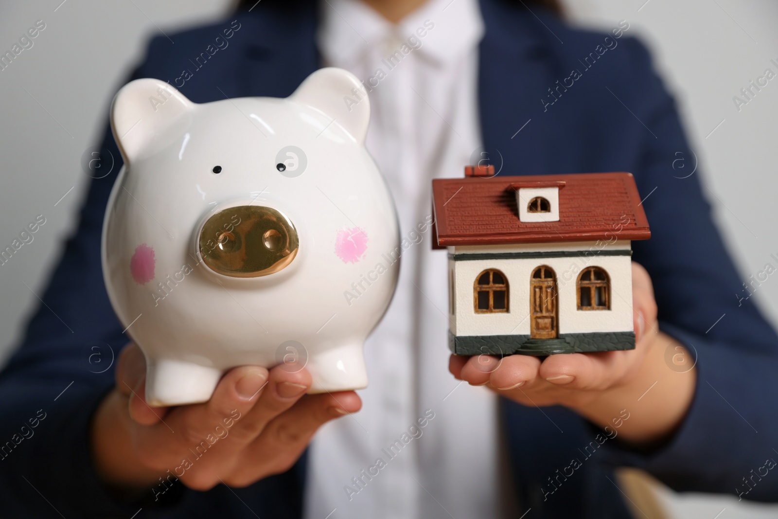 Photo of Woman holding piggy bank and little house model on light grey background, closeup