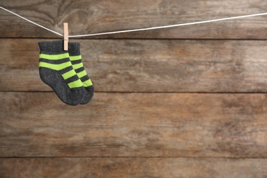 Photo of Pair of socks on laundry line against wooden background, space for text. Baby accessories