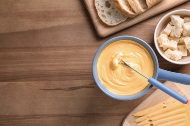 Flat lay composition with cheese fondue and bread on wooden table, space for text