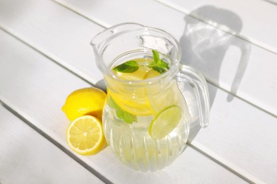 Jug of water with lemons and mint on white wooden table, above view