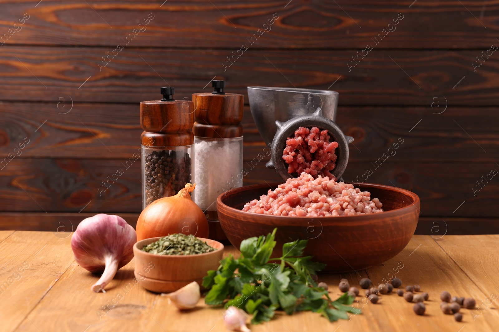 Photo of Manual meat grinder with beef mince, spices and parsley on wooden table