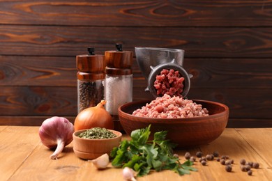 Manual meat grinder with beef mince, spices and parsley on wooden table