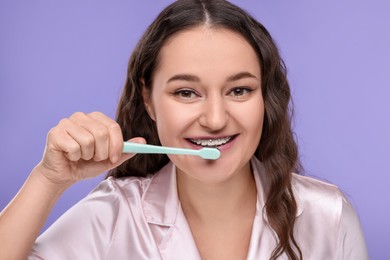 Photo of Woman with braces cleaning teeth on violet background