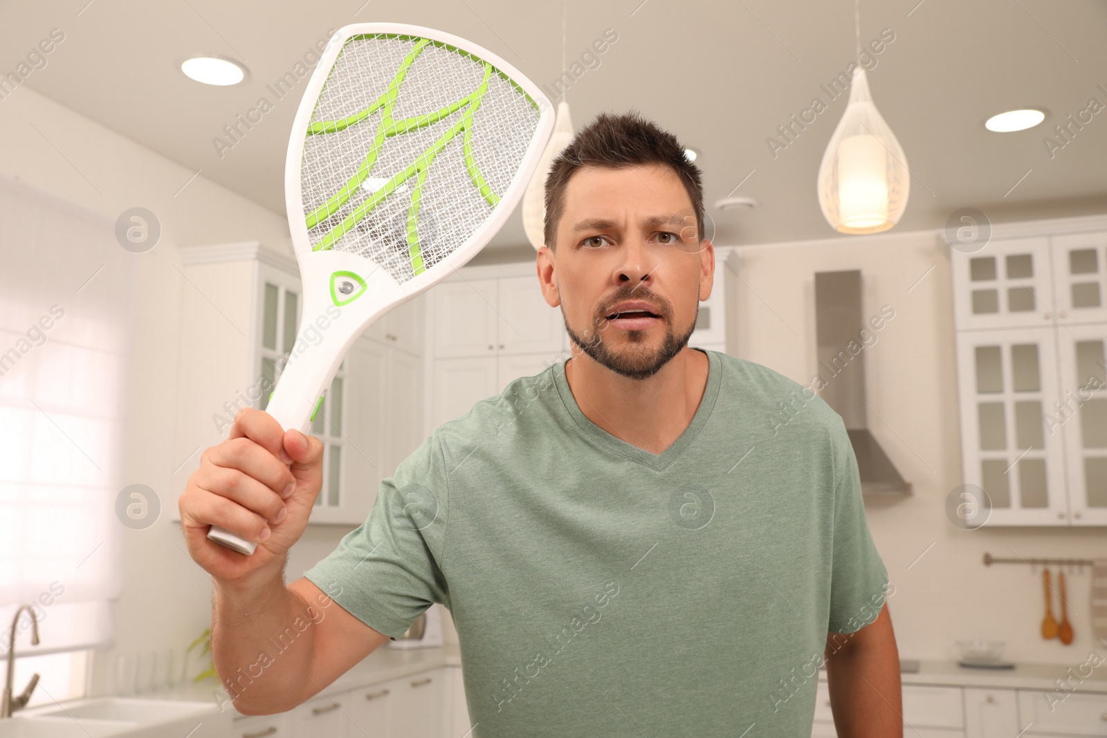 Photo of Man with electric fly swatter in kitchen. Insect killer