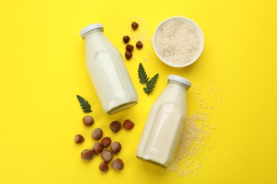 Photo of Vegan milks, hazelnuts and rice on yellow background, flat lay