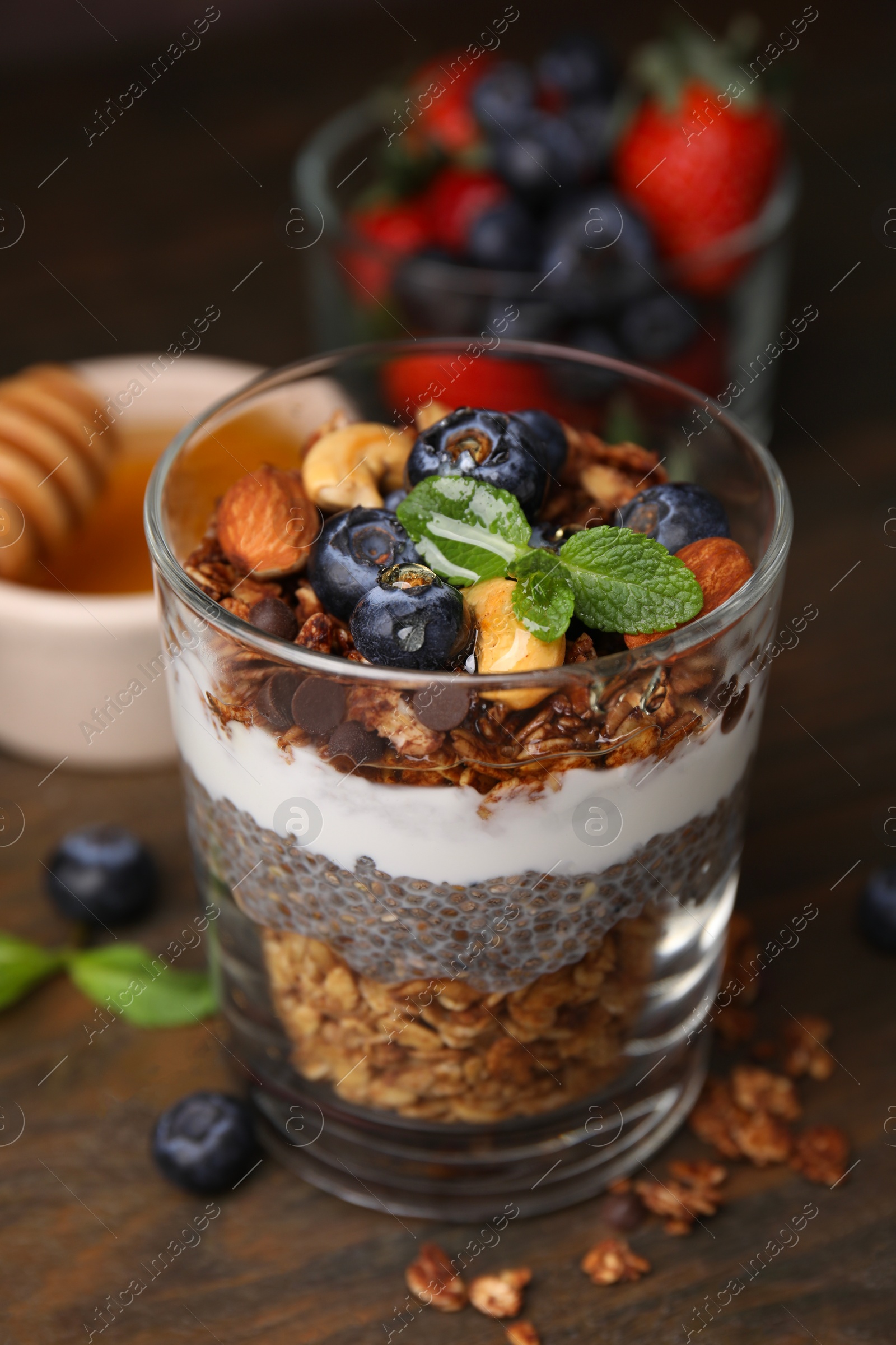 Photo of Tasty granola with berries, nuts, yogurt and chia seeds in glass on wooden table, closeup