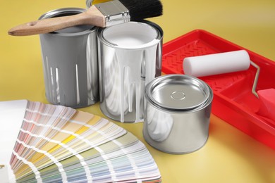 Photo of Cans of paints, brush, roller, tray and palette on yellow background