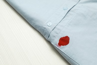 Photo of Shirt with stain of red ink on wooden table, closeup