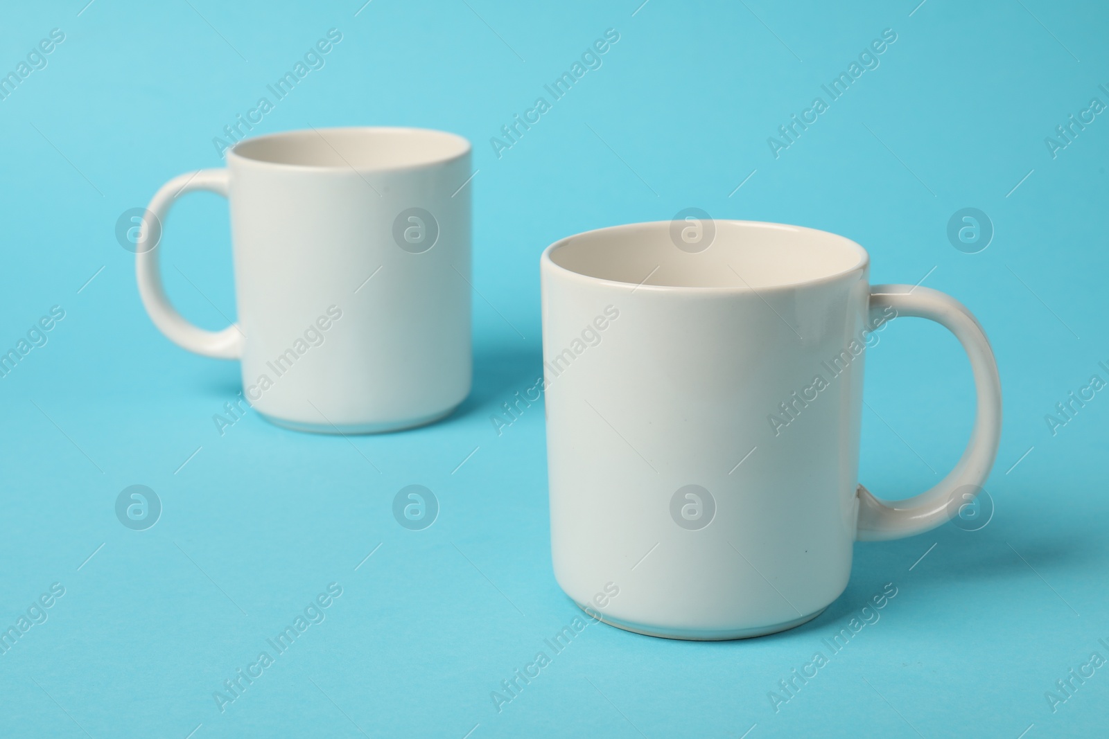 Photo of Two white ceramic mugs on light blue background