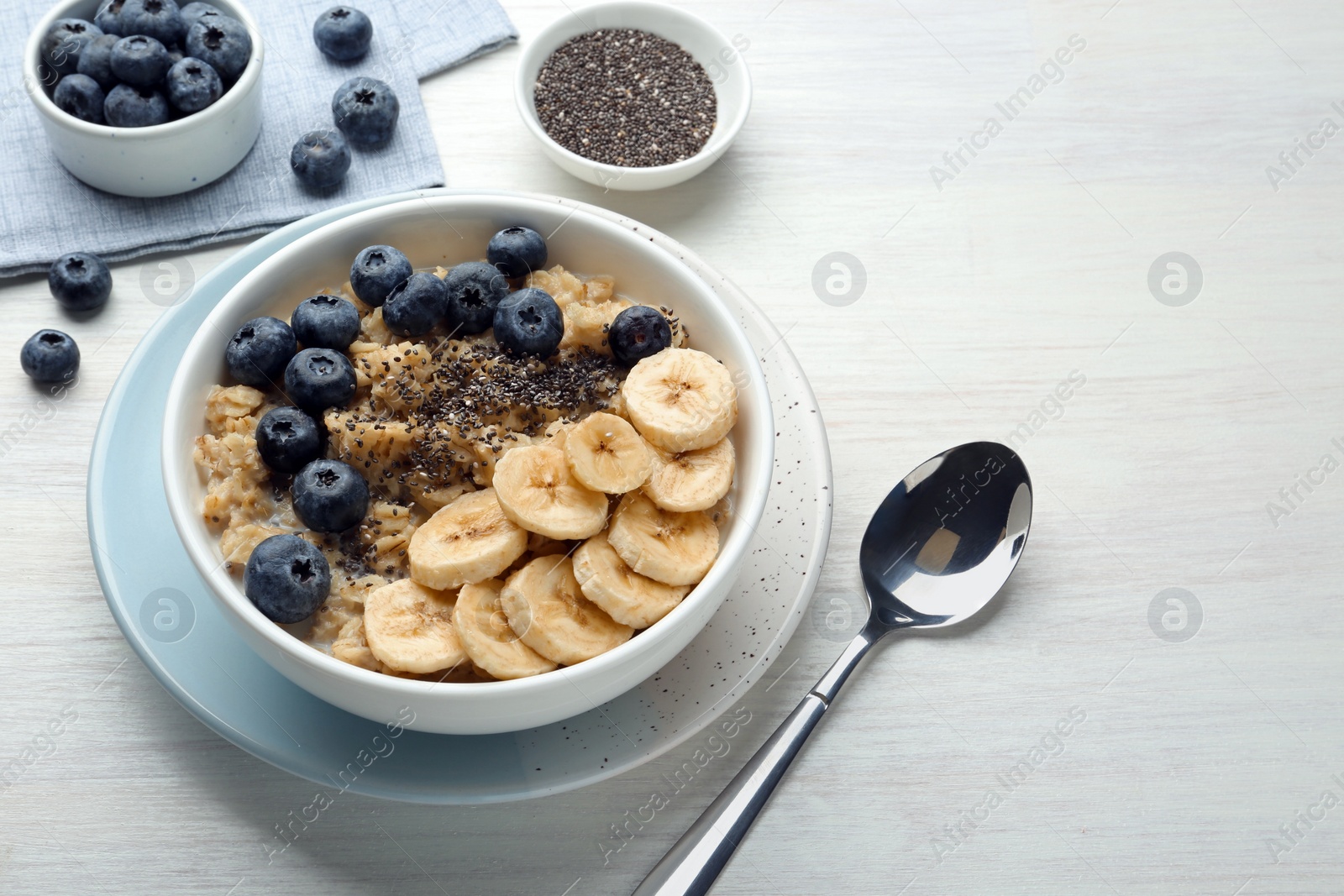 Photo of Tasty oatmeal with banana, blueberries and chia seeds served in bowl on white wooden table, space for text