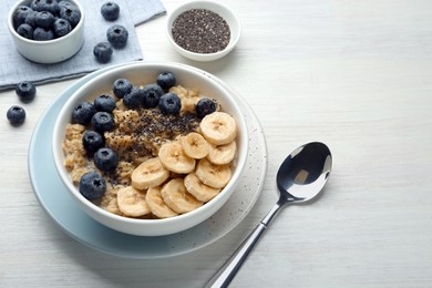 Photo of Tasty oatmeal with banana, blueberries and chia seeds served in bowl on white wooden table, space for text