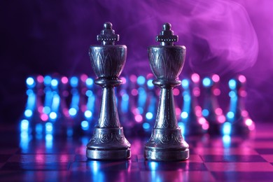 Photo of Kings in front of pawns on chessboard in color light, selective focus