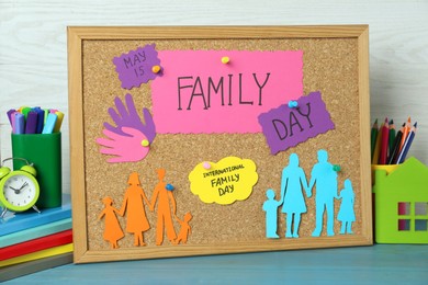 Photo of Cork board with text International Family Day and paper cutouts on light blue wooden table
