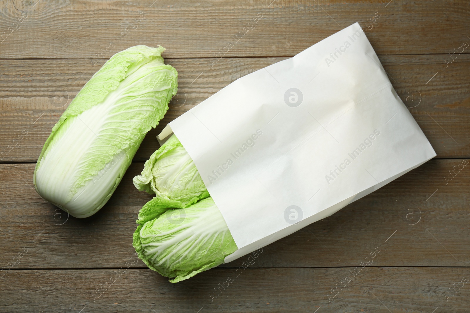 Photo of Fresh Chinese cabbages in paper bag on wooden table, top view