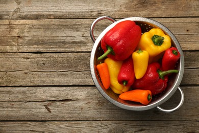 Photo of Metal colander with fresh peppers on wooden table, top view. Space for text