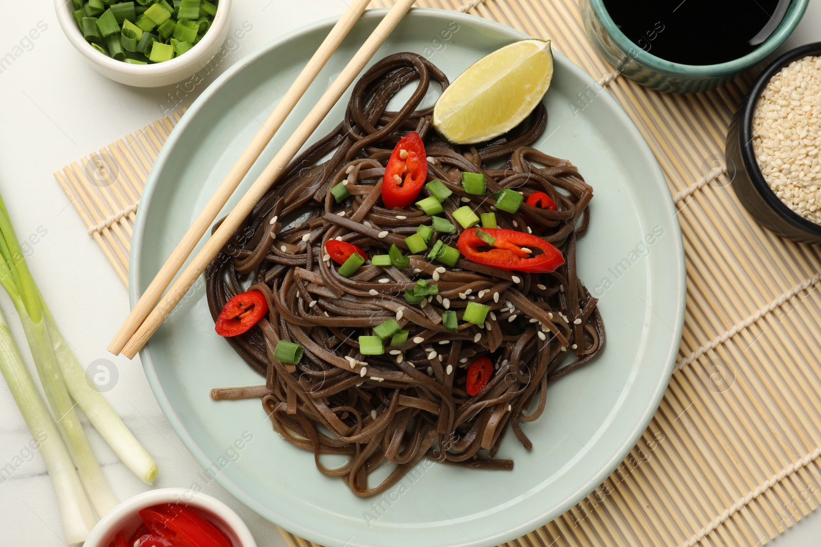 Photo of Tasty buckwheat noodles (soba) with onion served on white table, flat lay