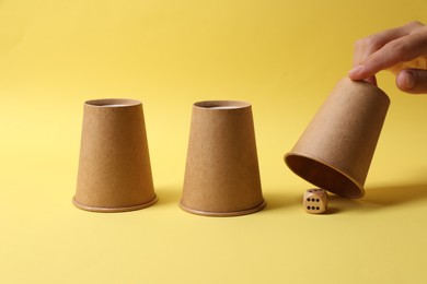 Photo of Woman showing dice under cup on yellow background, closeup. Thimblerig game