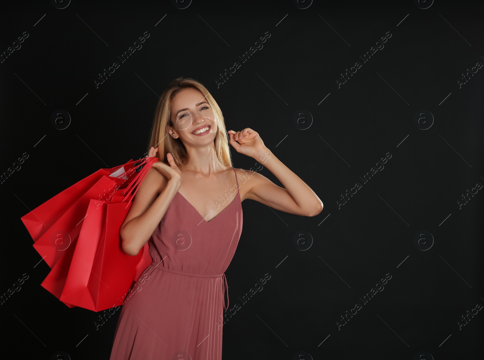 Photo of Happy young woman with shopping bags on dark background, space for text. Black Friday Sale