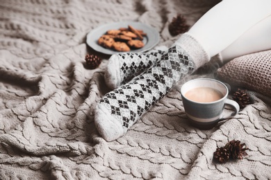 Woman wearing warm socks on knitted plaid, closeup. Cozy season