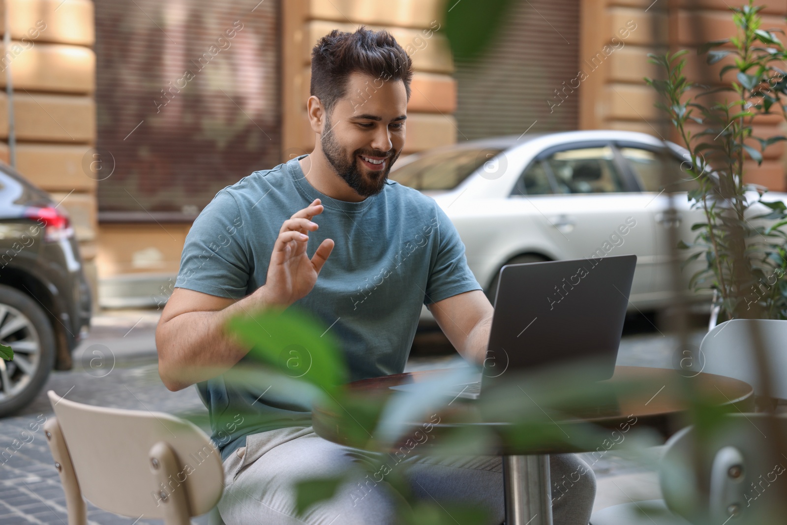 Photo of Handsome young man working on laptop at table in outdoor cafe