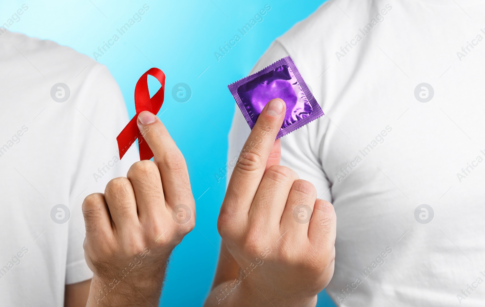 Photo of Men with condom and AIDS awareness ribbon on light blue background, closeup