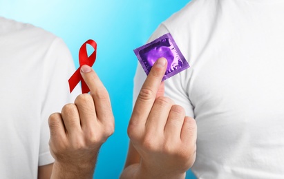 Men with condom and AIDS awareness ribbon on light blue background, closeup