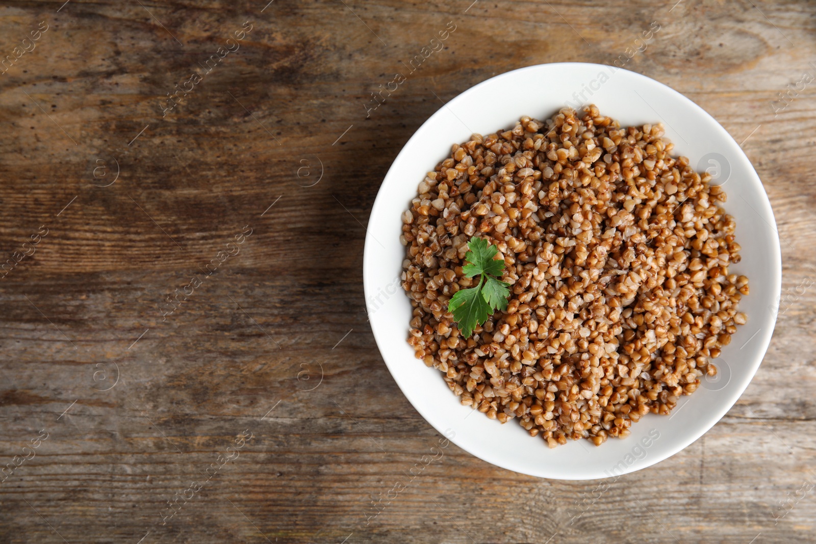 Photo of Dish of buckwheat porridge on wooden table, top view. Space for text