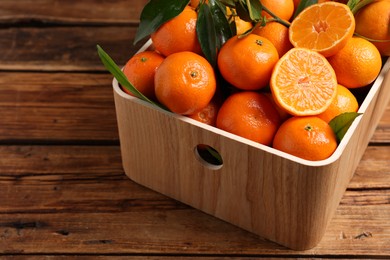 Photo of Fresh tangerines with green leaves in crate on wooden table, closeup