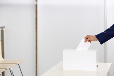 Man putting his vote into ballot box at polling station, closeup. Space for text