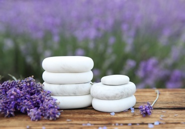 Photo of Spa stones, fresh lavender flowers and bath salt on wooden table outdoors, closeup