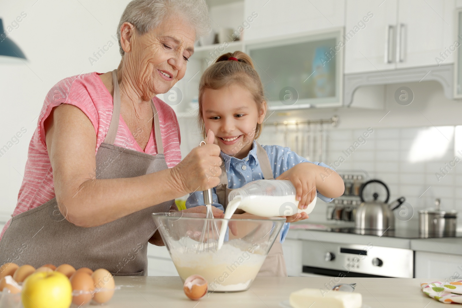 Photo of Cute girl and her grandmother cooking in kitchen