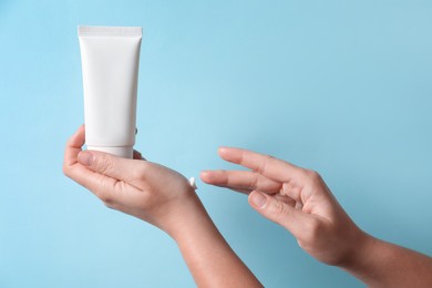 Photo of Woman with tube applying cosmetic cream onto her hand on light blue background, closeup