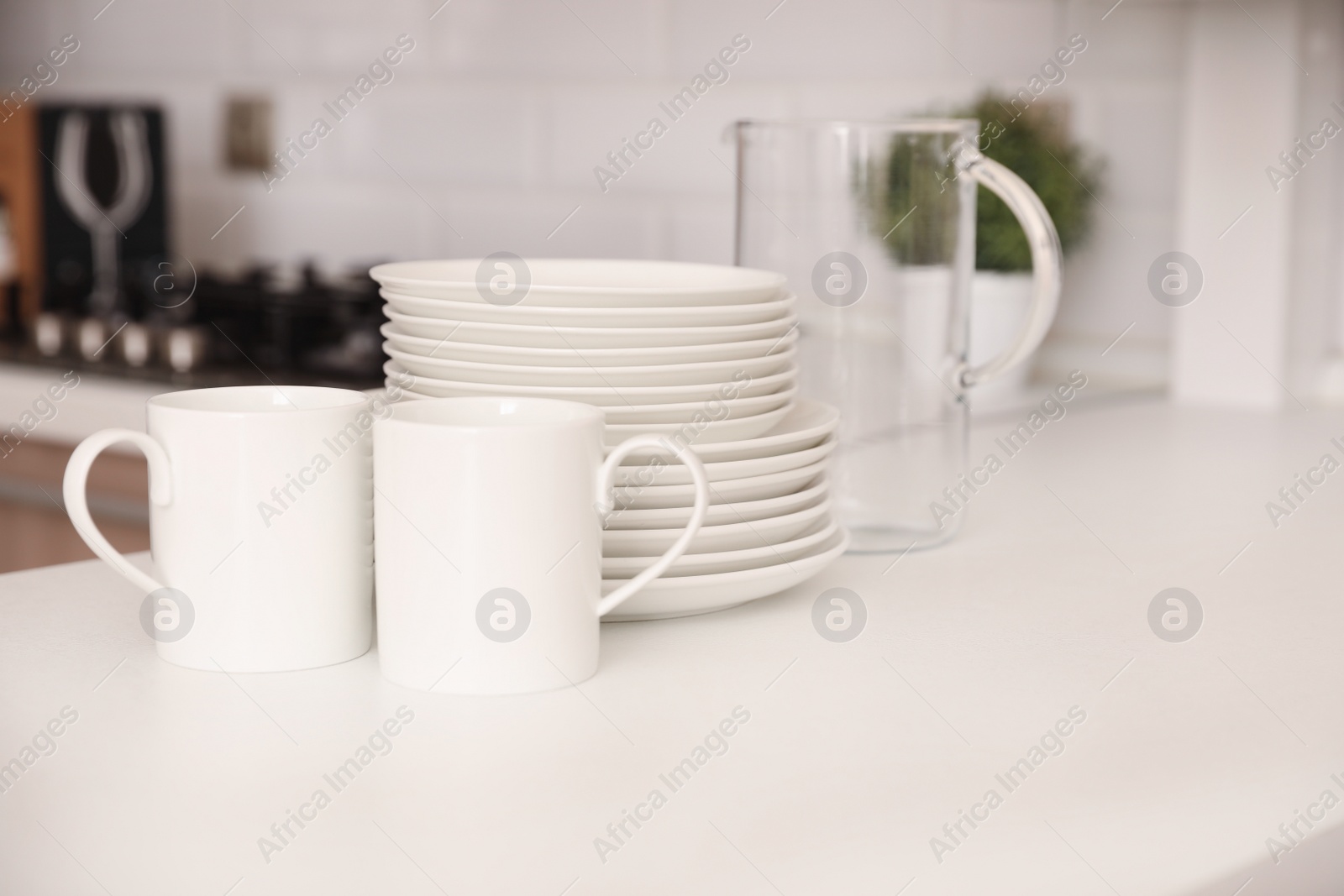 Photo of Stack of clean dishes, cups and glass jug on table in kitchen