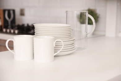 Photo of Stack of clean dishes, cups and glass jug on table in kitchen